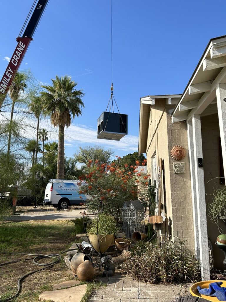 A crane lifting an HVAC unit over a residential house for installation or replacement by Hicken Air in Gilbert, AZ