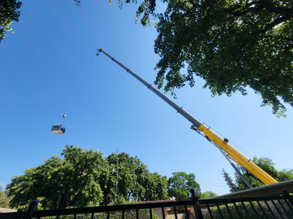 A crane lifting an HVAC unit over trees during an installation by All Pro Air in Warrenville, IL.