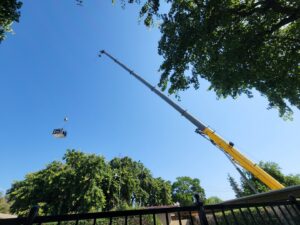A crane lifting an HVAC unit over trees during an installation by All Pro Air in Warrenville, IL.