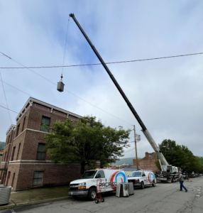 A crane lifting an HVAC unit with Pacifico Heating and Cooling service vans parked nearby in Shadyside, OH.