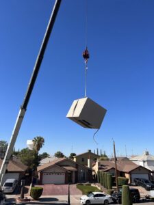 A crane lifting an HVAC unit over residential homes for installation or replacement by Anchor Air in El Paso, TX