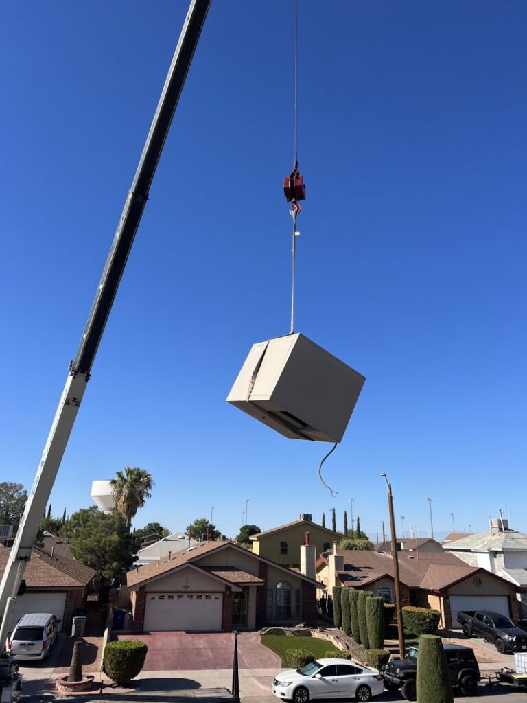 A crane lifting an HVAC unit over residential homes for installation or replacement by Anchor Air in El Paso, TX