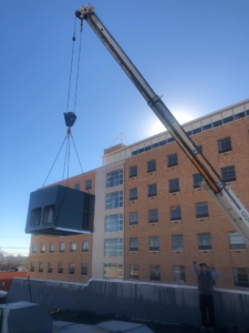 A crane lifting a new HVAC unit onto a commercial building roof for installation by Dr. Cool Heating and Cooling LLC in Roswell, NM.