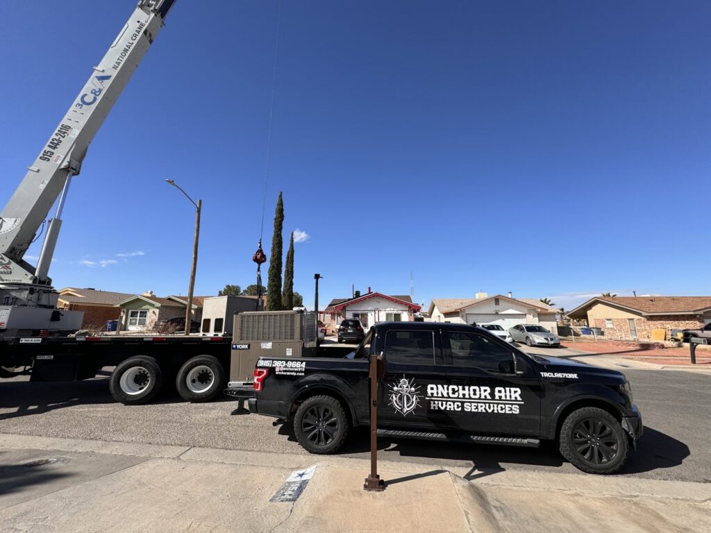 A crane lifting a large HVAC unit for installation, with an Anchor Air service truck nearby in El Paso, TX
