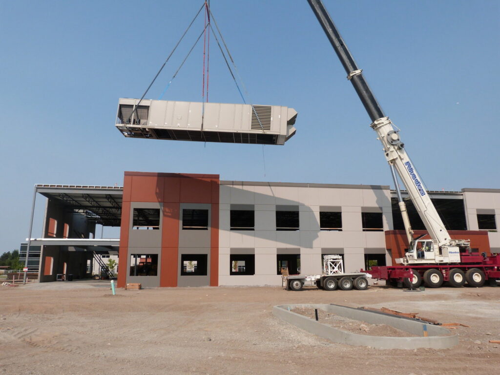 A crane lifting a large commercial HVAC unit onto a building under construction, performed by R&R Heating & Air Conditioning in Spokane, WA.