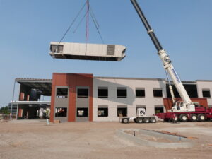 A crane lifting a large commercial HVAC unit onto a building under construction, performed by R&R Heating & Air Conditioning in Spokane, WA.