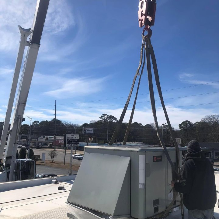 A crane lifting a large commercial HVAC unit onto a rooftop for installation or replacement by Eleven Heating and Cooling in Birmingham, AL.