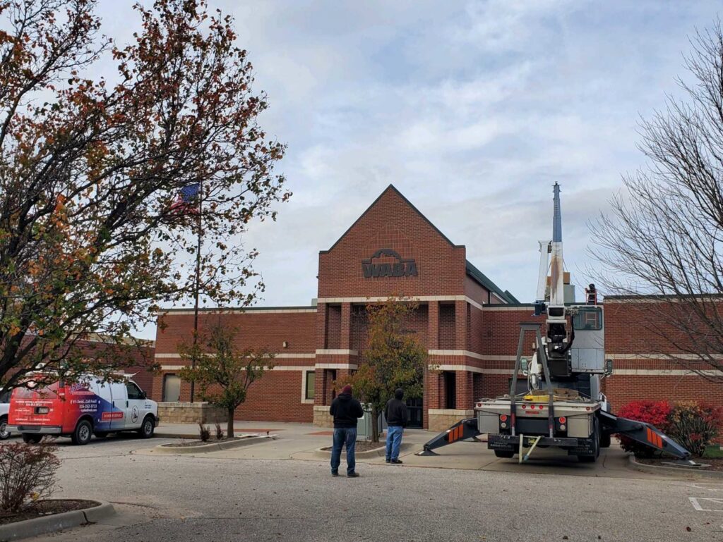 A crane lifting a new commercial HVAC unit onto a building rooftop for Frederick Plumbing, Heating & Air Conditioning in Wichita, KS