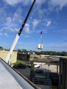 A crane lifting a new commercial HVAC unit onto a rooftop for installation by McGuffee's Air Conditioning and Heating in Gulfport, MS