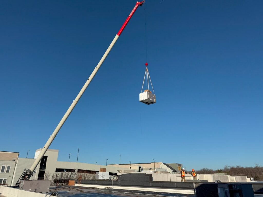 A crane lifting a new HVAC unit onto a rooftop with technicians present for APEX HVAC Solutions LLC in Frederick, MD.