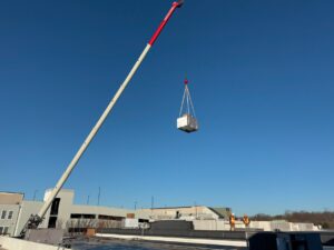 A crane lifting a new HVAC unit onto a rooftop with technicians present for APEX HVAC Solutions LLC in Frederick, MD.