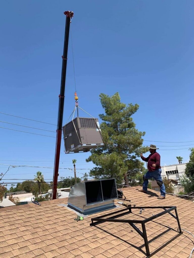 A crane lifting a new residential HVAC unit onto a roof, guided by a worker from BH cooling & Heating in Glendale, AZ.