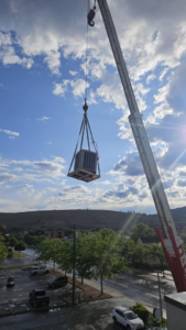 A crane lifting a new rooftop AC unit into place for JL Mechanical in Pleasant Grove, UT.