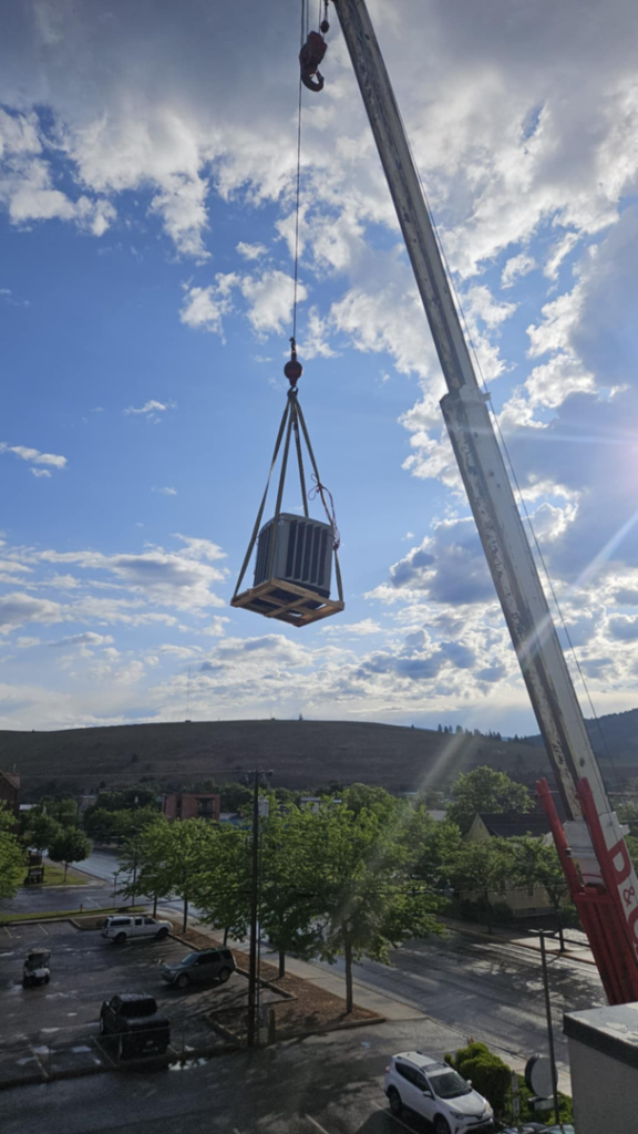 A crane lifting a new rooftop AC unit into place for JL Mechanical in Pleasant Grove, UT.
