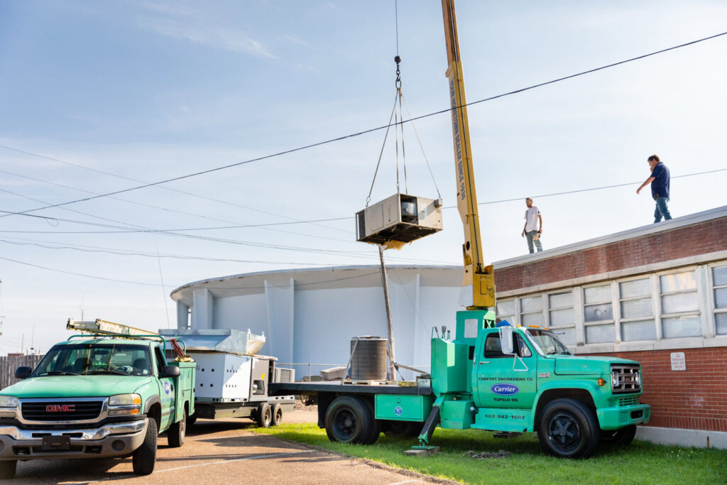 A crane lifting a new HVAC unit onto a commercial rooftop, installed by Comfort Engineering Co Inc in Tupelo, MS