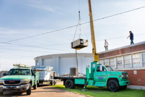 A crane lifting a new HVAC unit onto a commercial rooftop, installed by Comfort Engineering Co Inc in Tupelo, MS