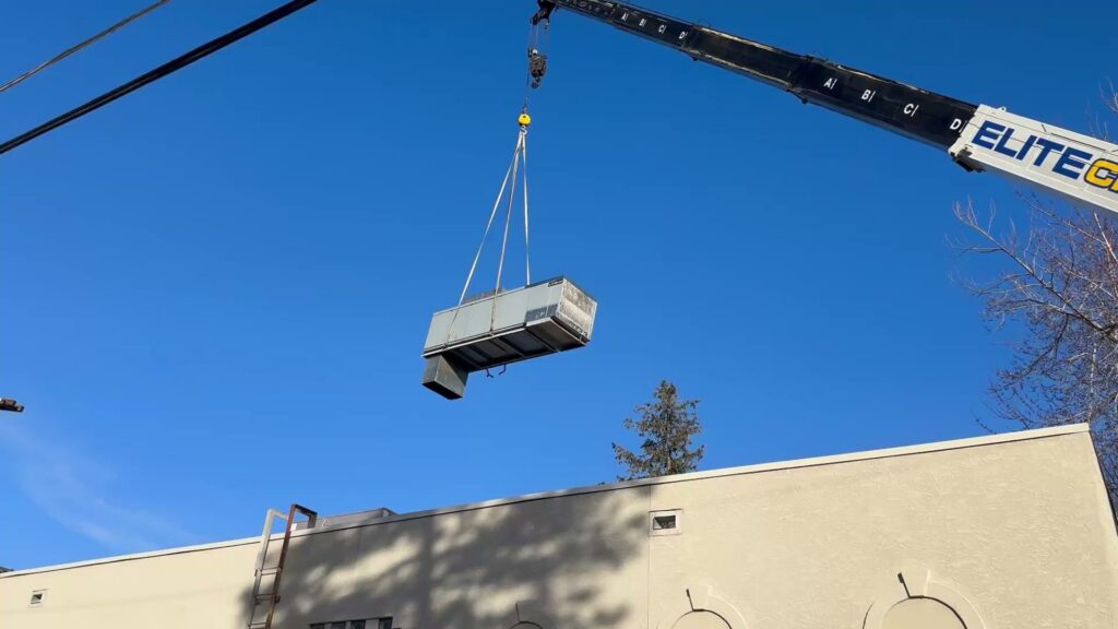 A crane lifting a new rooftop HVAC unit into place during installation by CHAMPS Heating&Air in Denver, CO