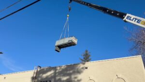 A crane lifting a new rooftop HVAC unit into place during installation by CHAMPS Heating&Air in Denver, CO