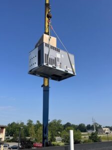 A large commercial HVAC unit being lifted by a crane onto a rooftop for installation by Jons-Air in Carmel, IN.