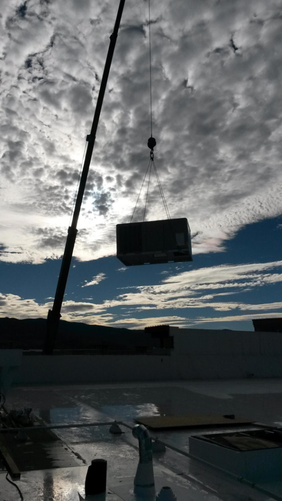 A crane lifting a large rooftop HVAC unit for installation on a commercial building by Proficient Heating & Air Conditioning llc in Livonia, MI.