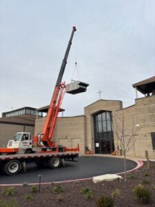 A crane lifting a new rooftop HVAC unit onto a commercial building, installed by R.J. O'Neil Inc. in Montgomery, IL.