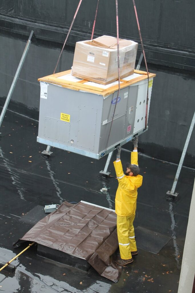 A worker guiding a large rooftop HVAC unit being lifted by a crane during an installation by RSC Heating and Air Conditioning in Lancaster, PA.