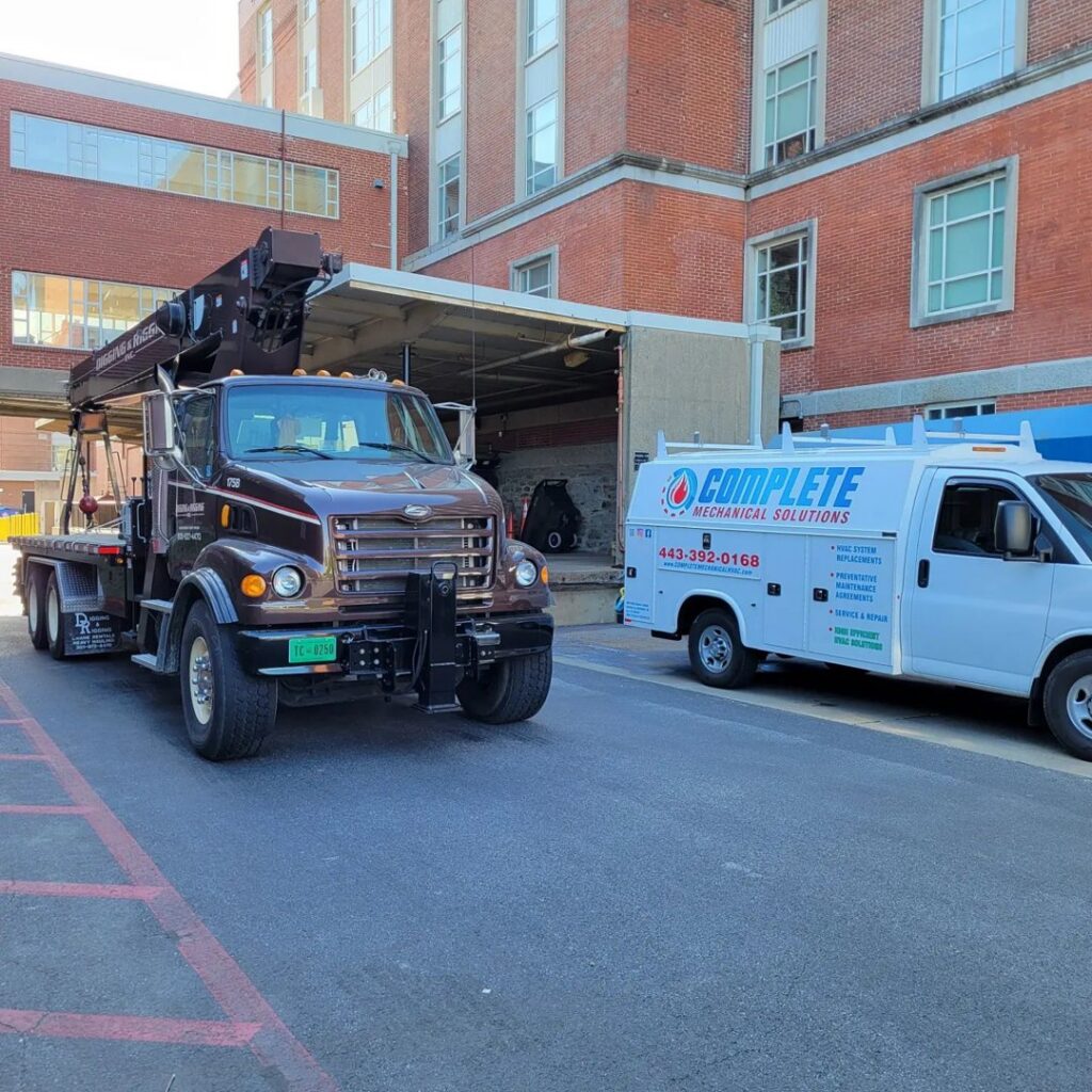 A crane truck and service van at a commercial job site for Complete Mechanical Solutions in Novi, MI.