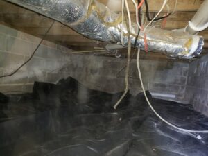 A crawl space with a newly installed black vapor barrier for moisture and pest control by Absolute Exterminating Services in Ellenwood, GA.