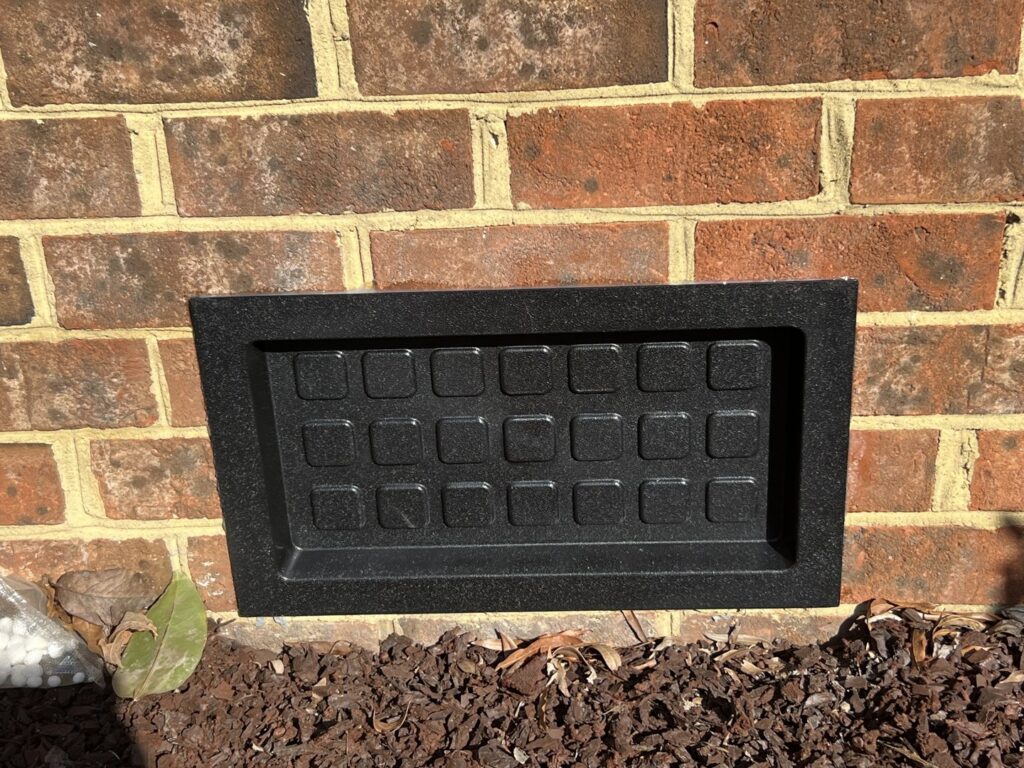 A new black crawl space vent cover installed on a brick foundation by Perry Crawl Space & Pest Control Solutions LLC in Chesapeake, VA.