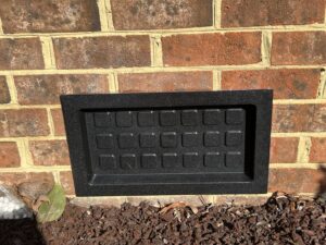 A new black crawl space vent cover installed on a brick foundation by Perry Crawl Space & Pest Control Solutions LLC in Chesapeake, VA.