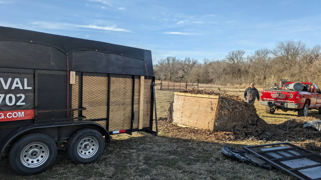 A Redline Mowing & Trimming crew loading leaf and yard debris onto a trailer during a property cleanup in Stillwater, OK.