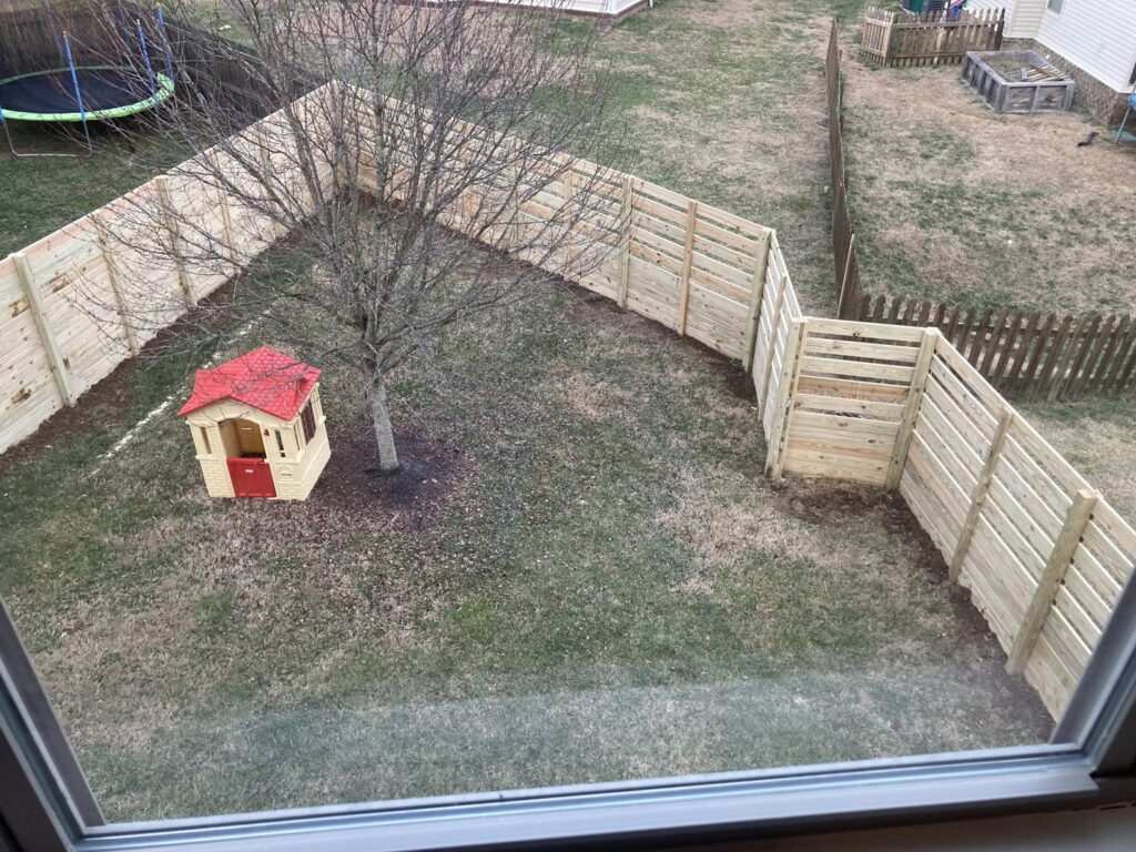 A curved horizontal slat wooden fence enclosing a backyard with a playhouse and trampoline by Fenceworks of Middle Tennessee in Nashville, TN.