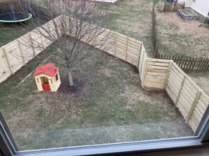 A curved horizontal slat wooden fence enclosing a backyard with a playhouse and trampoline by Fenceworks of Middle Tennessee in Nashville, TN.