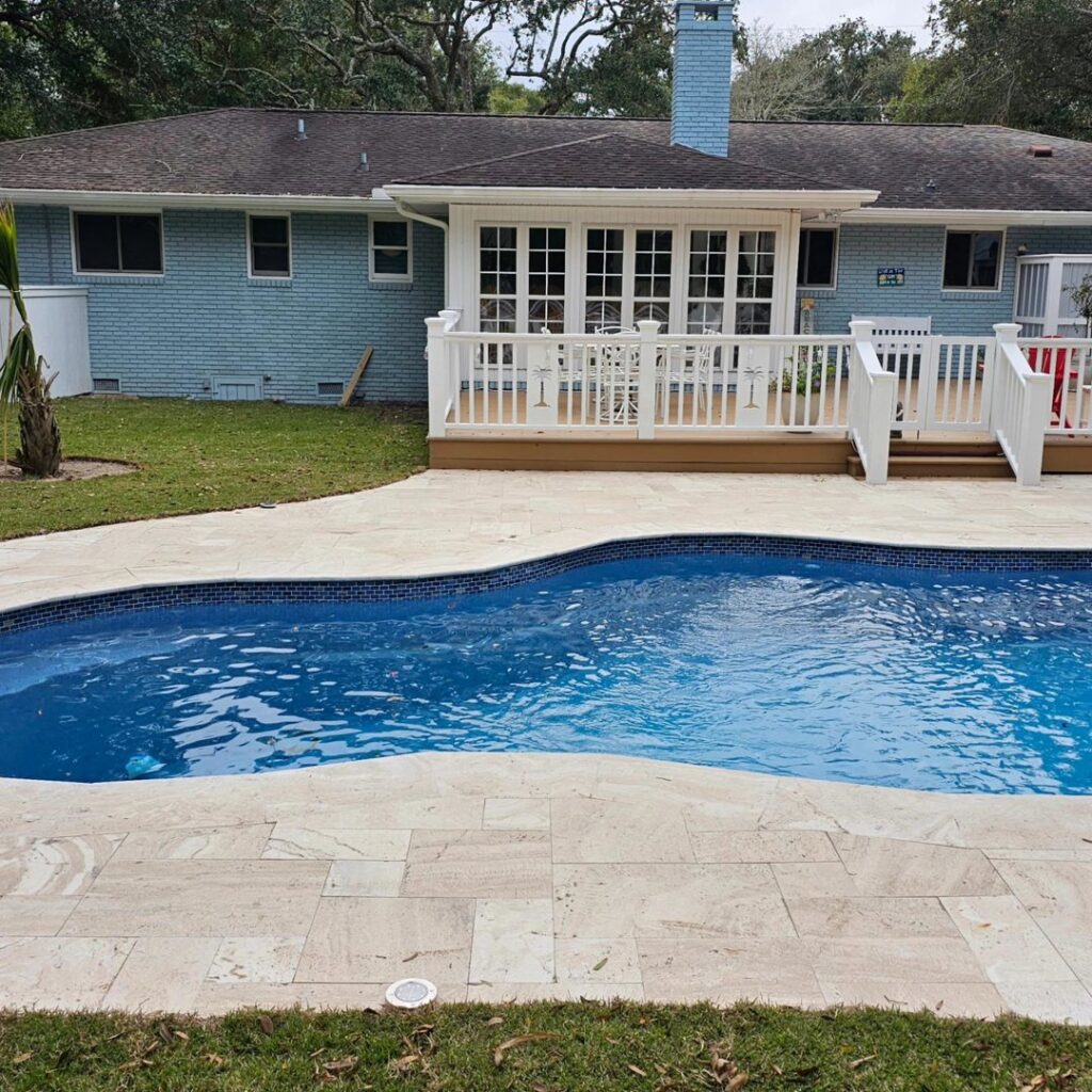 A curved swimming pool with a bright blue interior and light-colored paver decking, a project by Salty Reef Pools LLC in Summerville, SC.