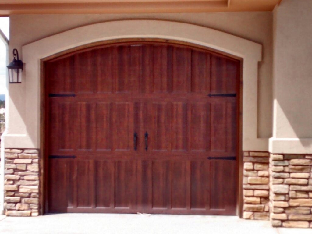 A custom arched wood-style garage door with decorative hardware installed by Mountain Fox Garage Doors in Colorado Springs, CO.