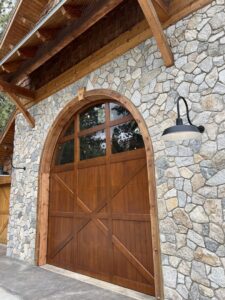 Custom arched wooden garage door with cross-brace design on a stone home, installed by Continental Door Company, Spokane Valley, WA.