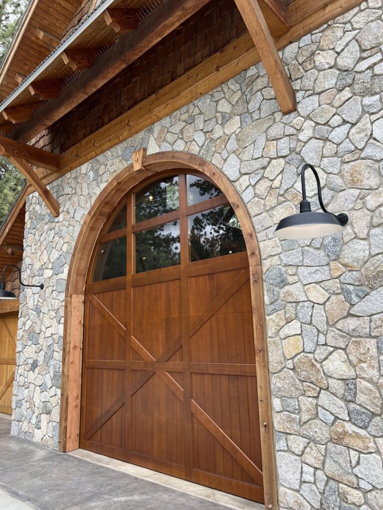 Custom arched wooden garage door with cross-brace design on a stone home, installed by Continental Door Company, Spokane Valley, WA.