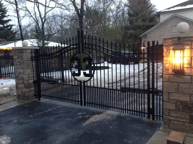 A custom-designed black metal driveway gate with stone pillars installed by Freeman Fence in Atlanta, GA.