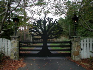 A custom black metal gate with a decorative tree design and stone pillars installed by United Fence Company in Johnston, RI.