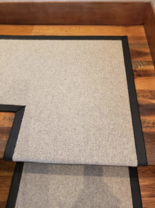 A close-up of a custom carpet runner with black binding on wooden stairs by Altered Edge in Kalispell, MT
