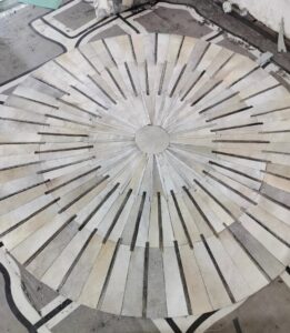 A custom circular rug made of light-colored strips being laid out on a floor, showcasing work by Makymo in Commerce, CA