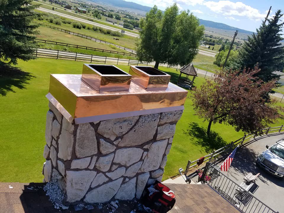Custom copper chimney cap and two square vents installed on a stone chimney by Butte Tin Shop, Inc. in Butte, MT.