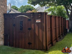 A custom dark stained wood fence with a decorative gate and top trim next to a pool area by Fence Defense in Plano, TX