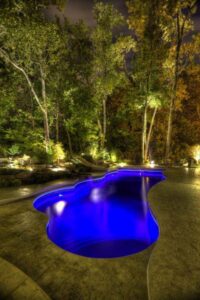 A custom-shaped inground pool illuminated with blue lights at night by Firemaster in Oklahoma City, OK