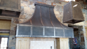 A custom dark metal range hood with decorative rivets installed in a kitchen by Bensley Sheet Metal in Bozeman, MT.