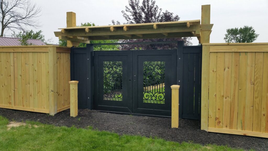 A custom ornamental gate with decorative elements and flanking wood fences, installed by Sharper Image Fence in Fort Wayne, IN.