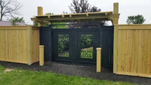 A custom ornamental gate with decorative elements and flanking wood fences, installed by Sharper Image Fence in Fort Wayne, IN.