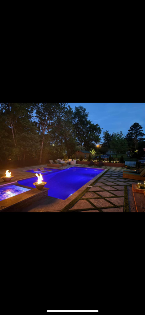 A custom pool featuring decorative fire bowls and ambient lighting at night, built by Luxury Outdoors in Murfreesboro, TN.