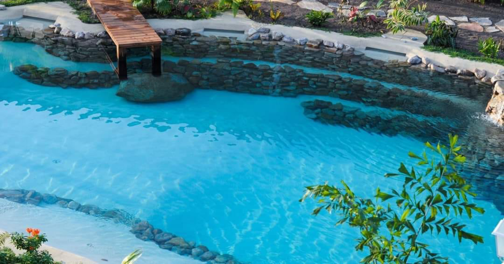 A custom-designed pool featuring a wooden bridge and natural rock features by The Staycation Builders in Fort Wayne, IN.