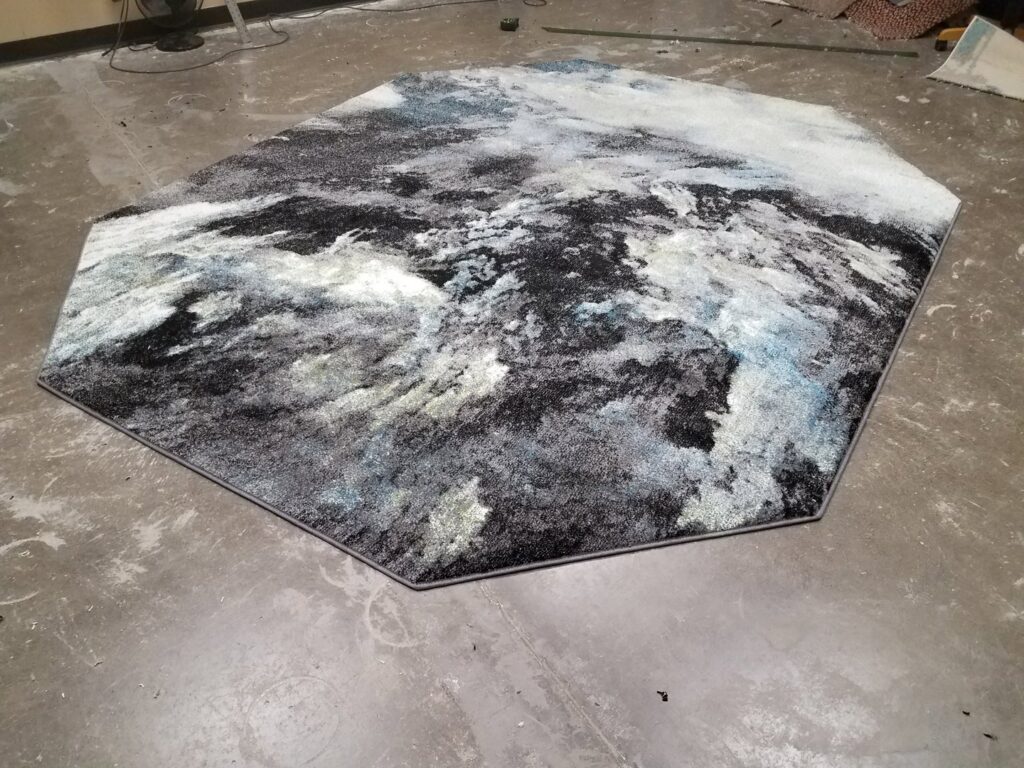A custom-shaped area rug with an abstract black, white, and blue pattern and bound edges by Carpet Binding By Scott in Oklahoma City, OK